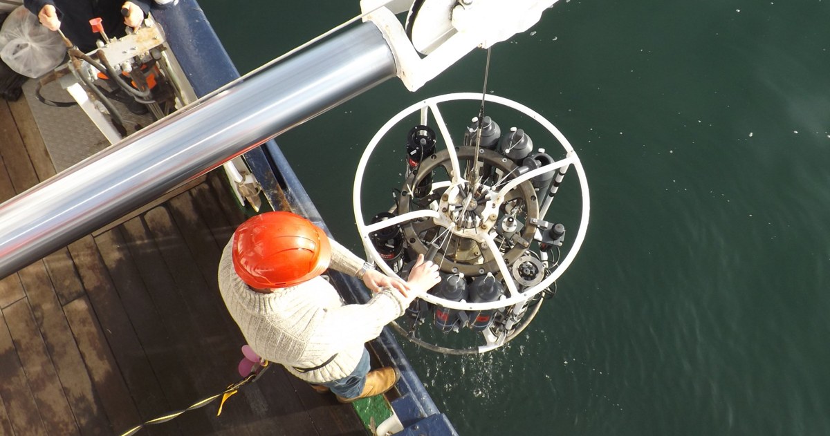 Ocean scientists on a research vessel deploying a CTD rosette sampler over the side